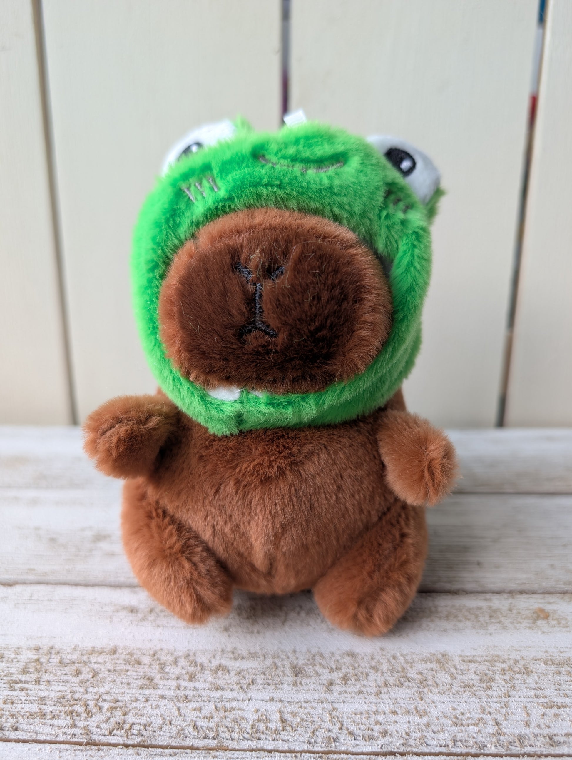 Fluffy capybara keychain plushy wearing green frog eyes hat.