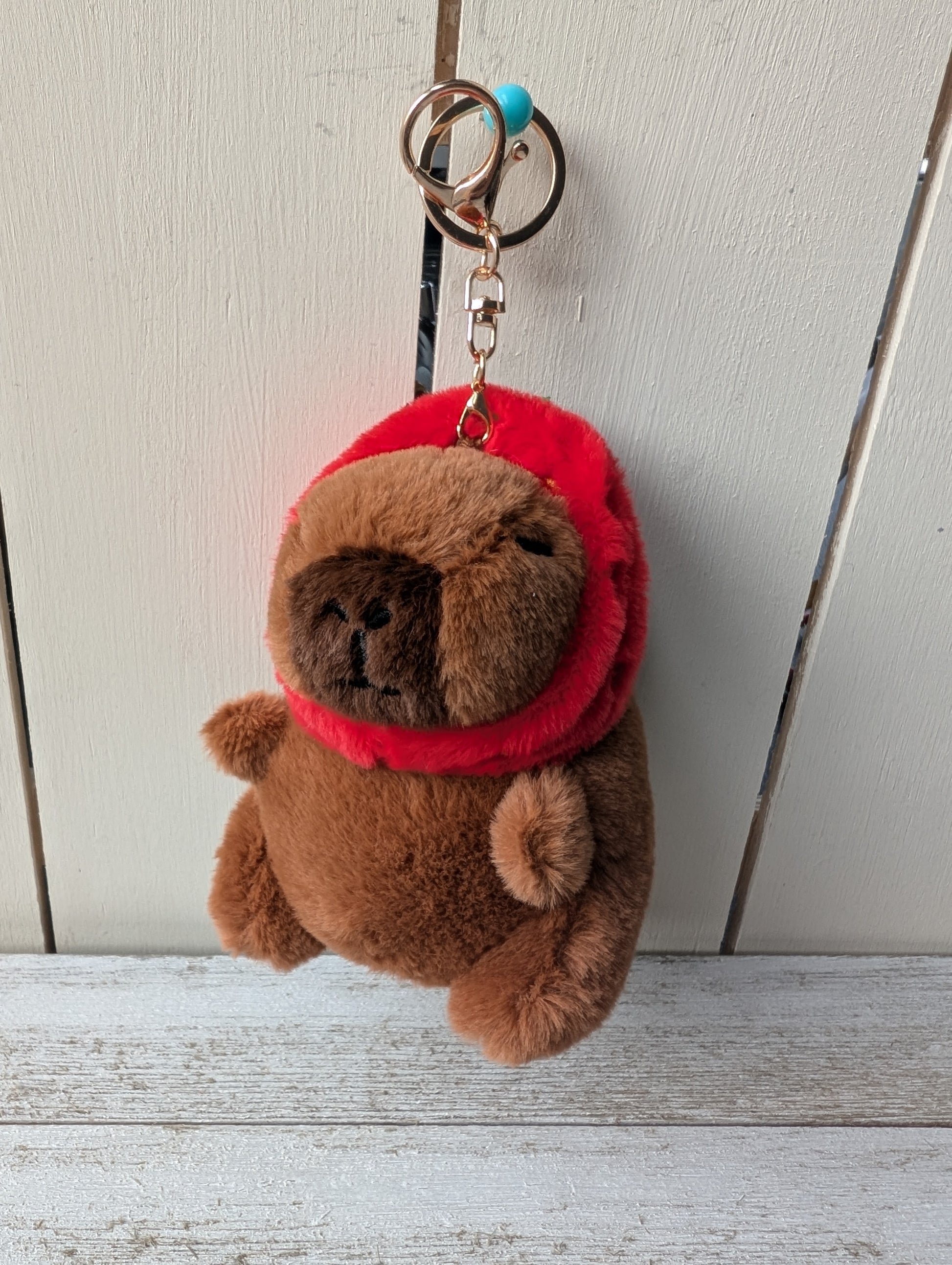 Plush capybara wearing strawberry hat keychain.