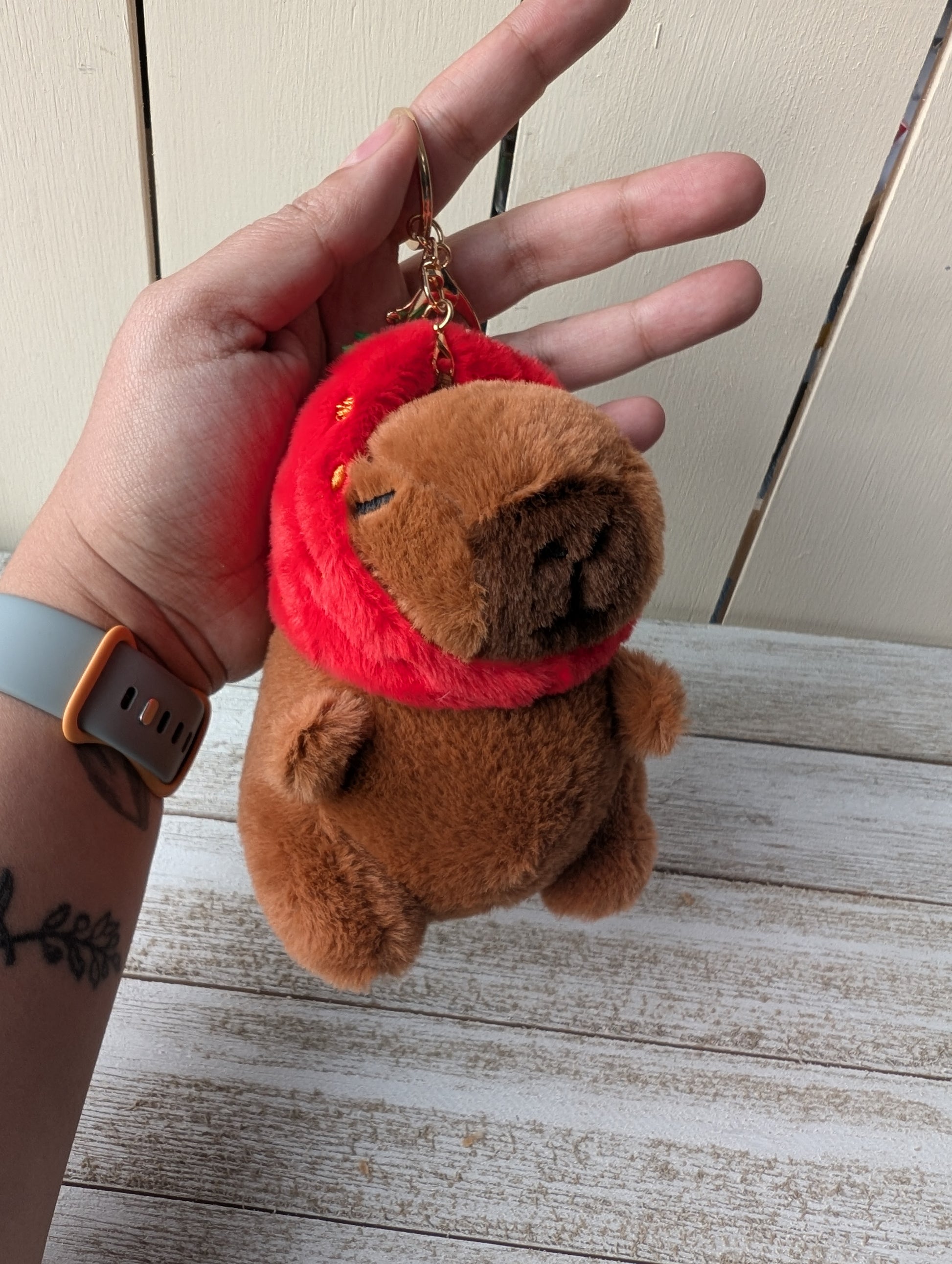Plush capybara wearing strawberry hat keychain.