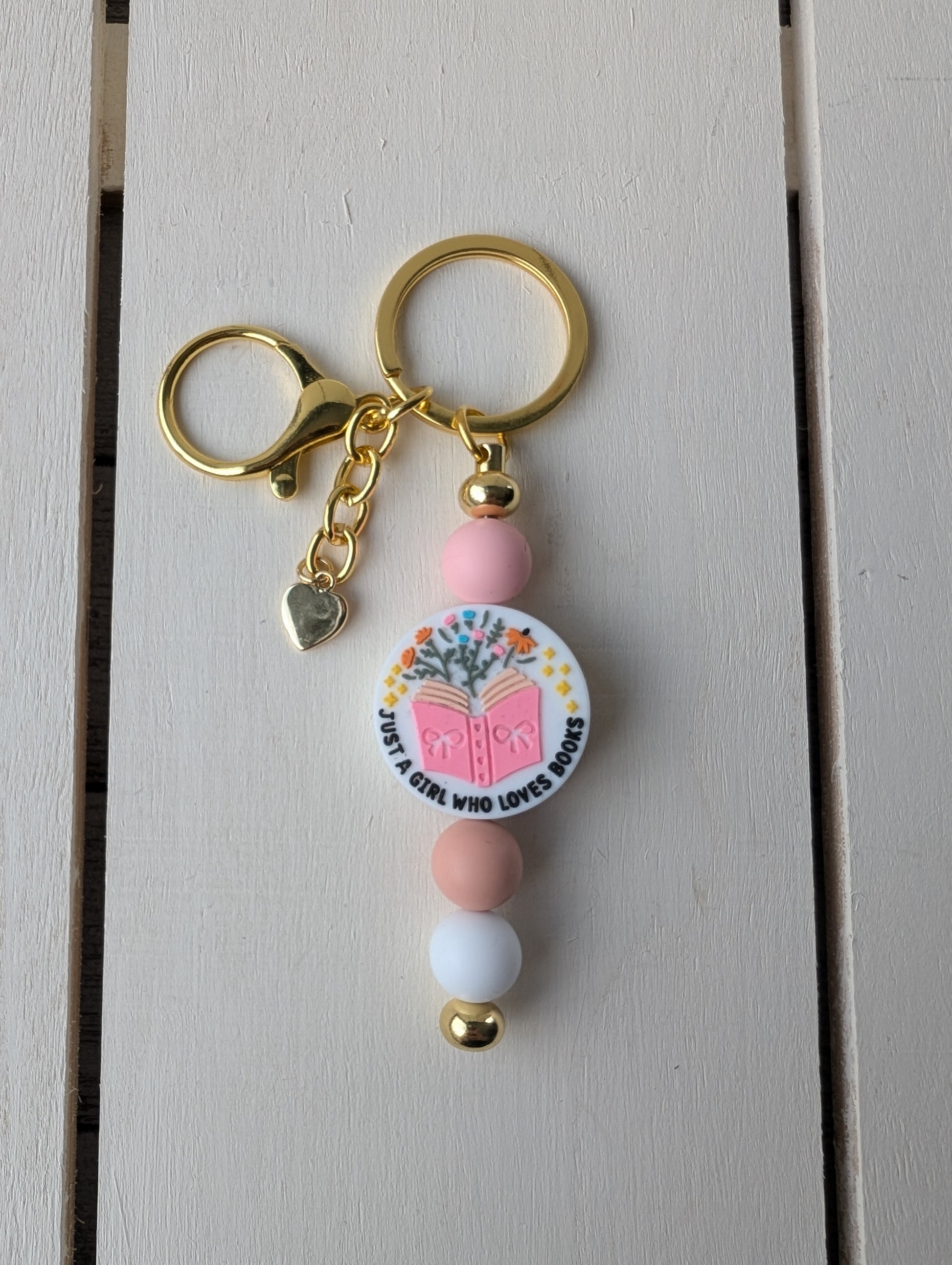 Gold bar keychain with "just a girl who loves books" focal bead between pink and tan silicone beads. Includes gold heart charm.