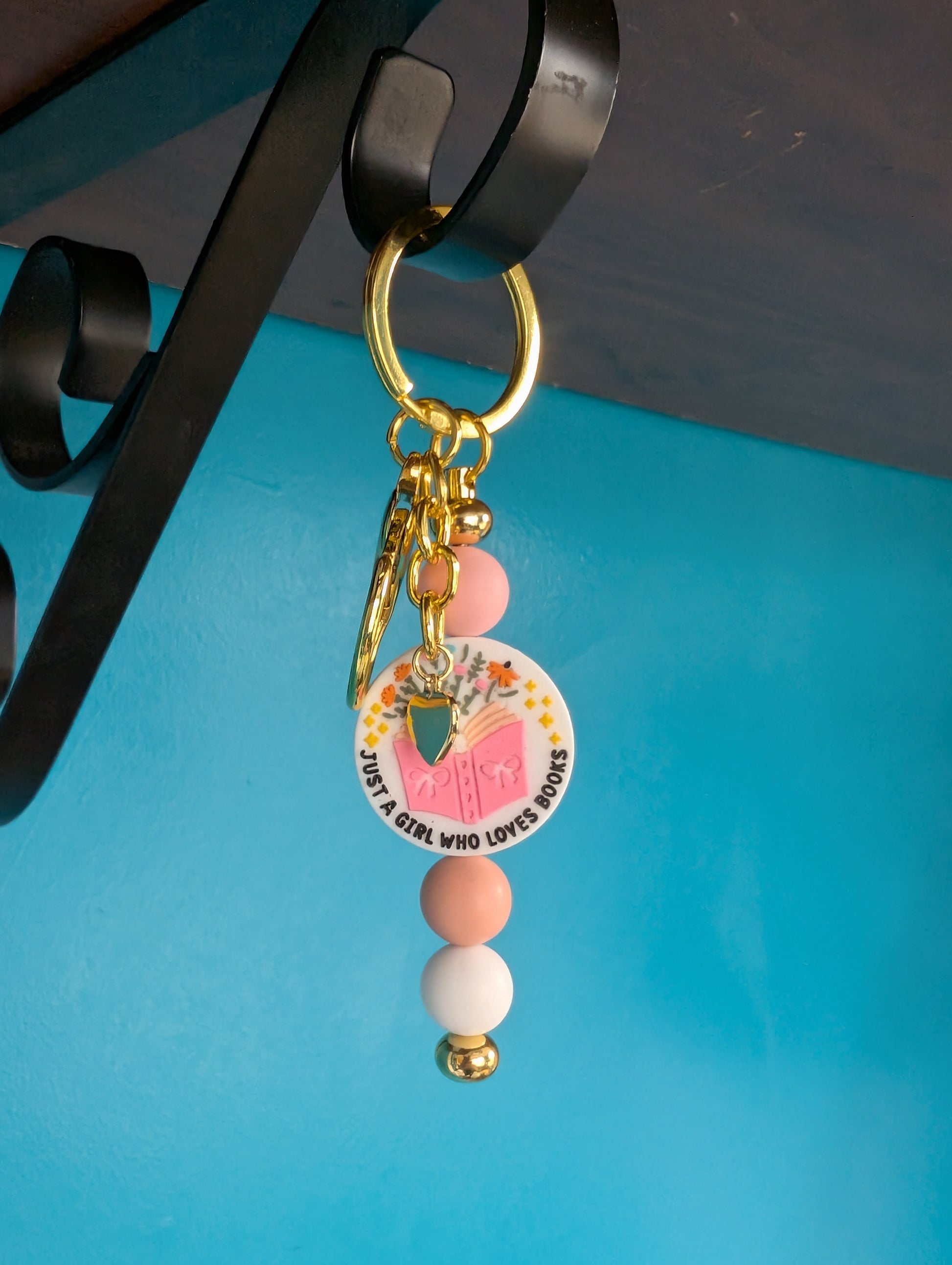 Gold bar keychain with "just a girl who loves books" focal bead between pink and tan silicone beads. Includes gold heart charm.