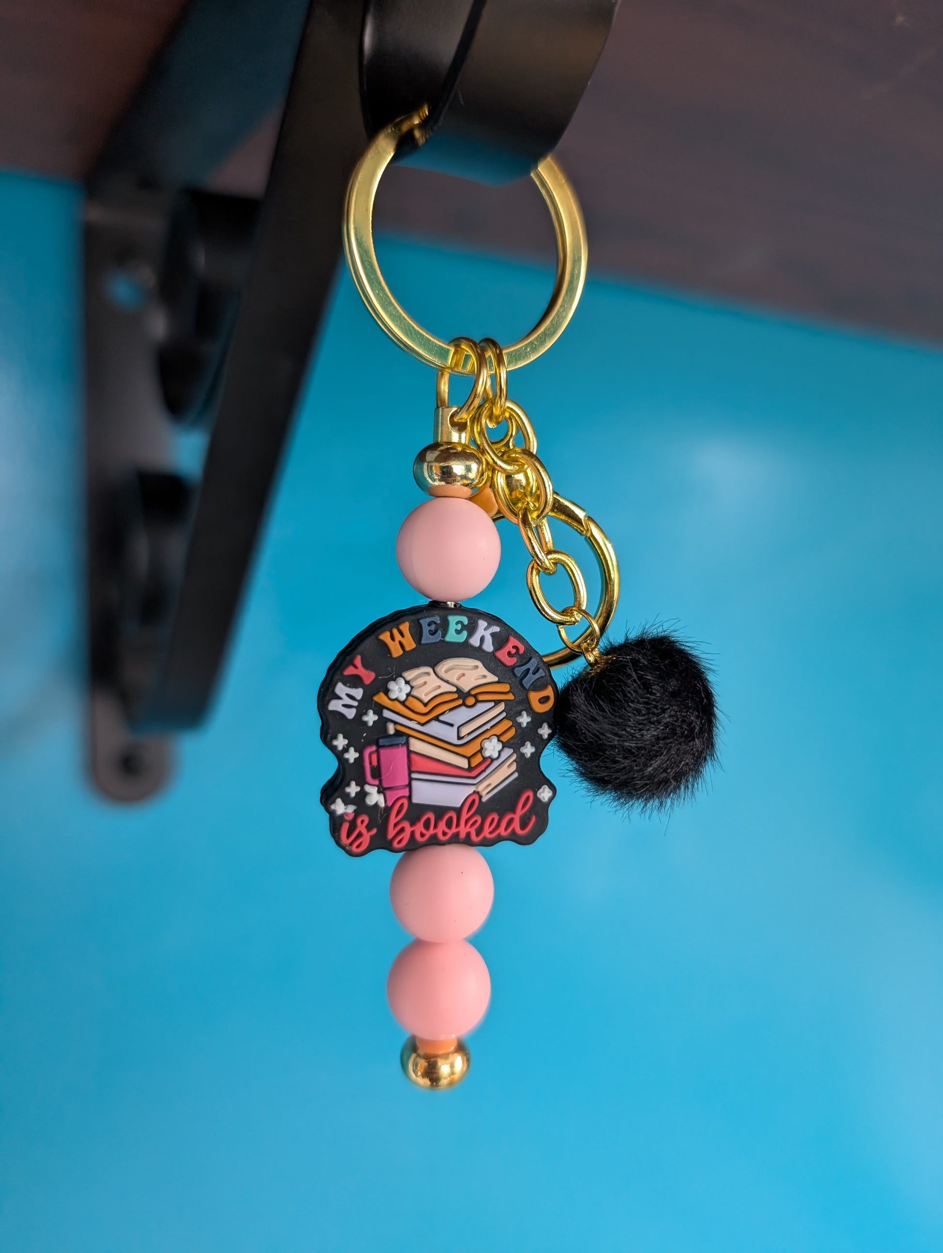 Gold keychain with pink beads and "my weekend is booked" focal bead. Includes black pompom charm.